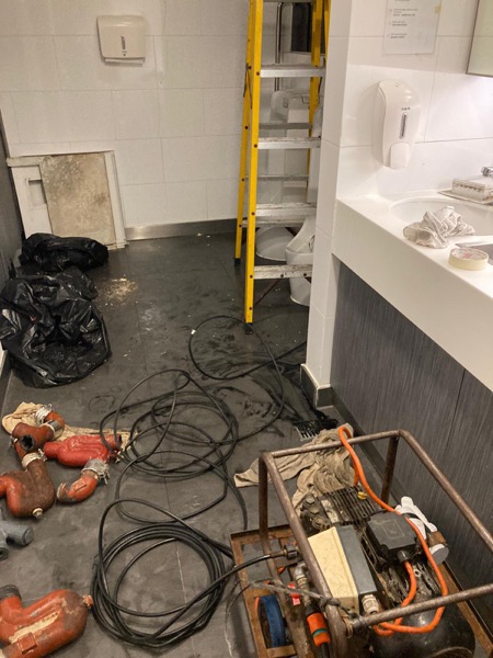 DrainFix HK 商業樓宇廁所現場，紅色鑄鐵 P-trap、電動通渠機、垃圾袋擺好預備工作