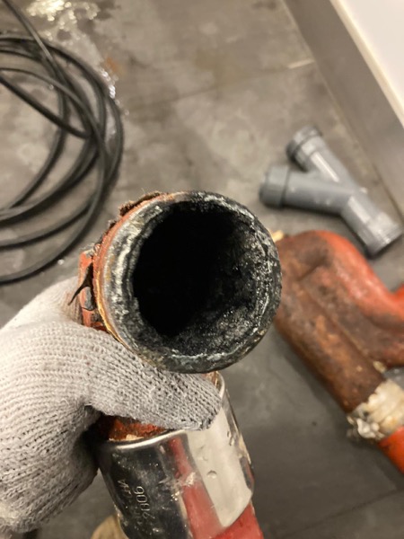 DrainFix HK 戴手套拎起一段崩咗嘅紅鑄鐵渠管末端，俾客戶睇損壞嚴重程度